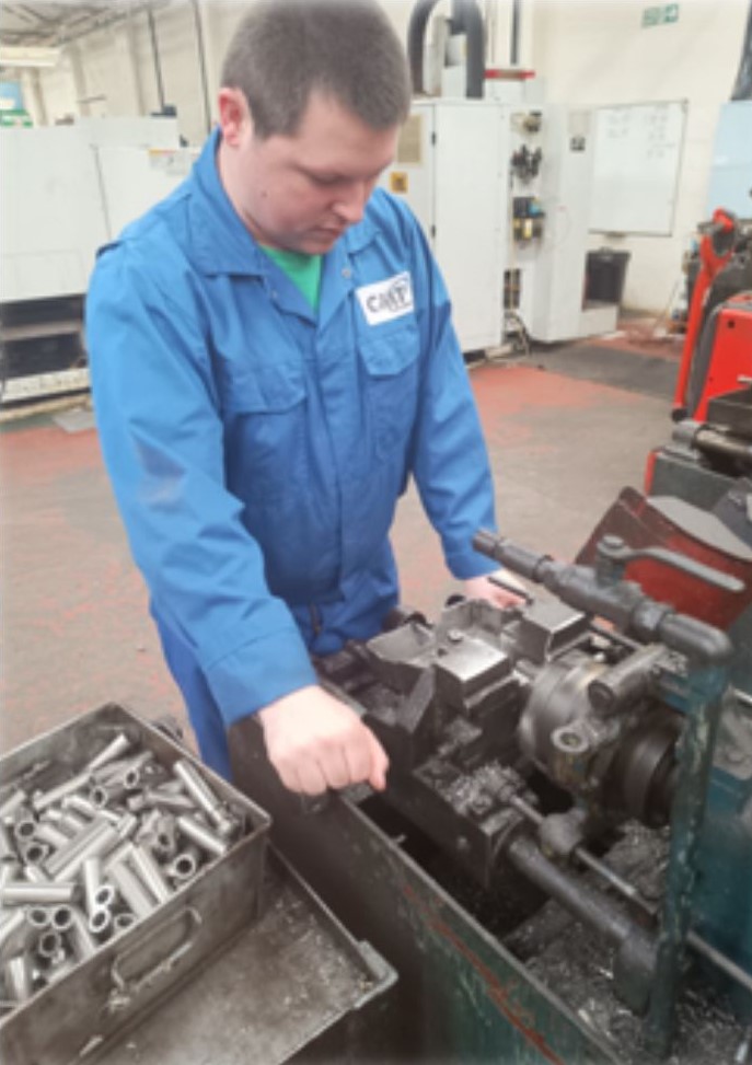 Sam Green in blue CMT overalls, at work at a machine at CMT Engineering